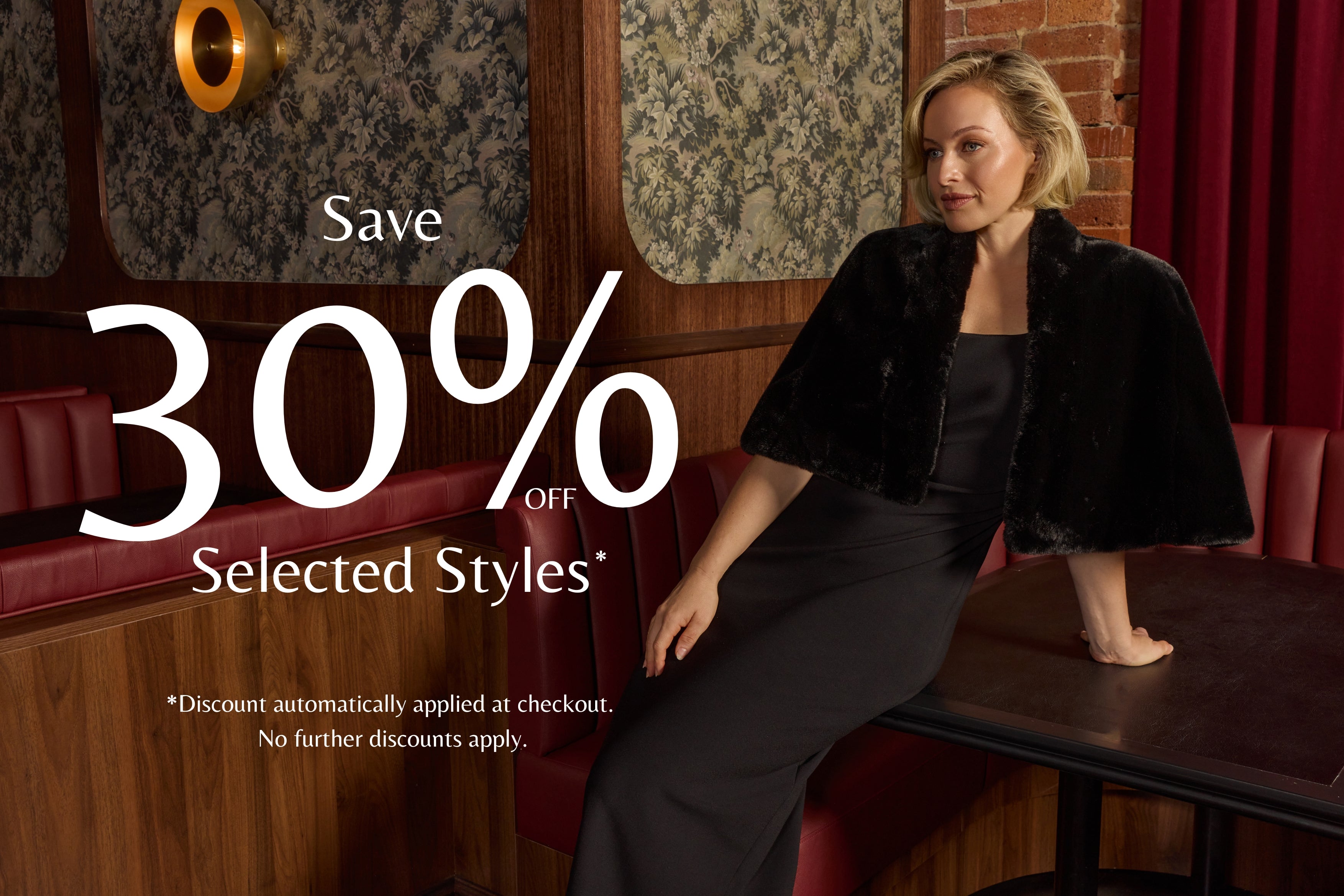 A woman in a black dress and black fur-trimmed cape jacket sits in a red leather booth in a restaurant or lounge setting, with large promotional text reading 'Save 30% Off Selected Styles' overlaid on the image.