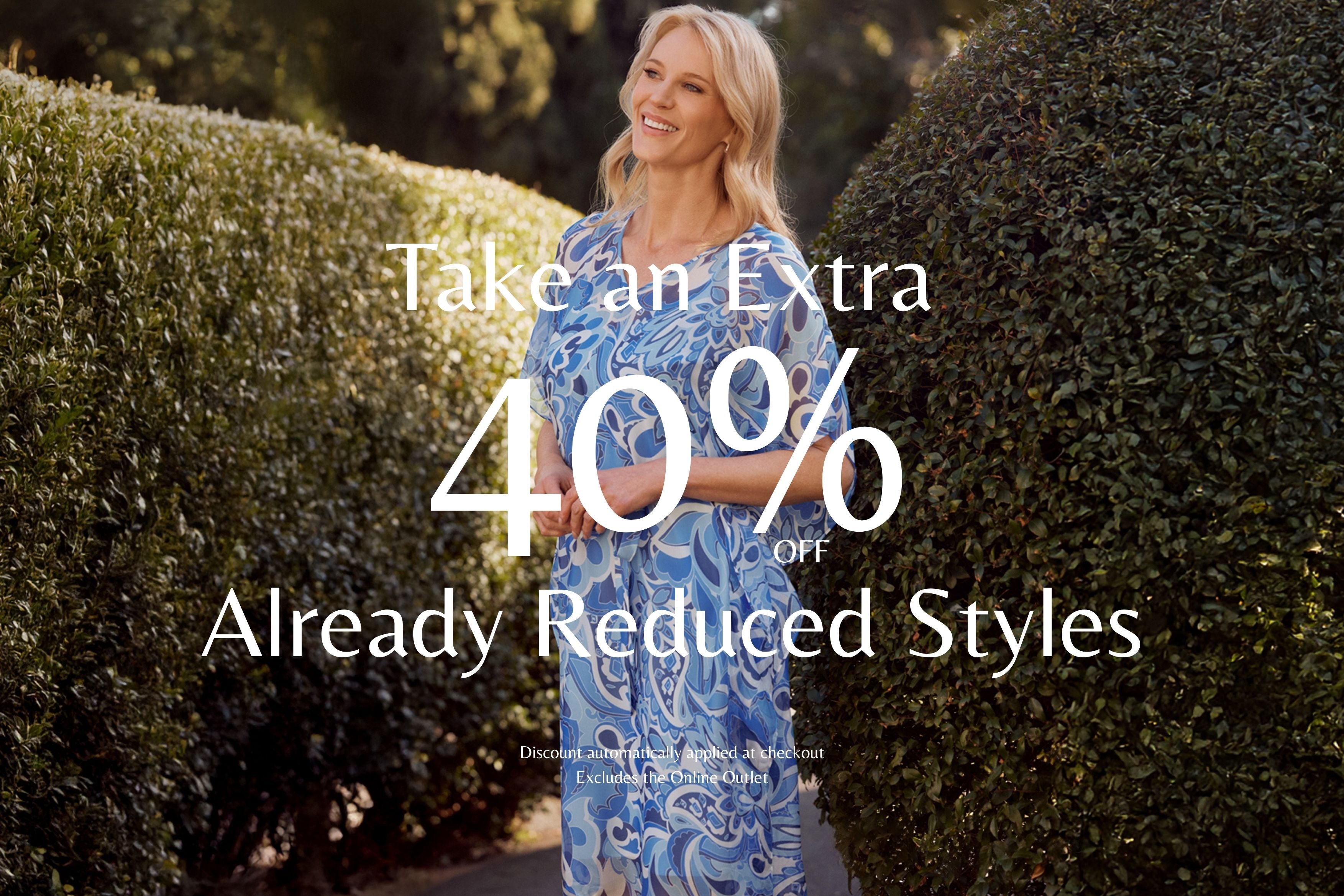 Woman in a blue dress standing between two hedges with promotional text overlay. Take an Extra 40% Off Already Reduced Styles