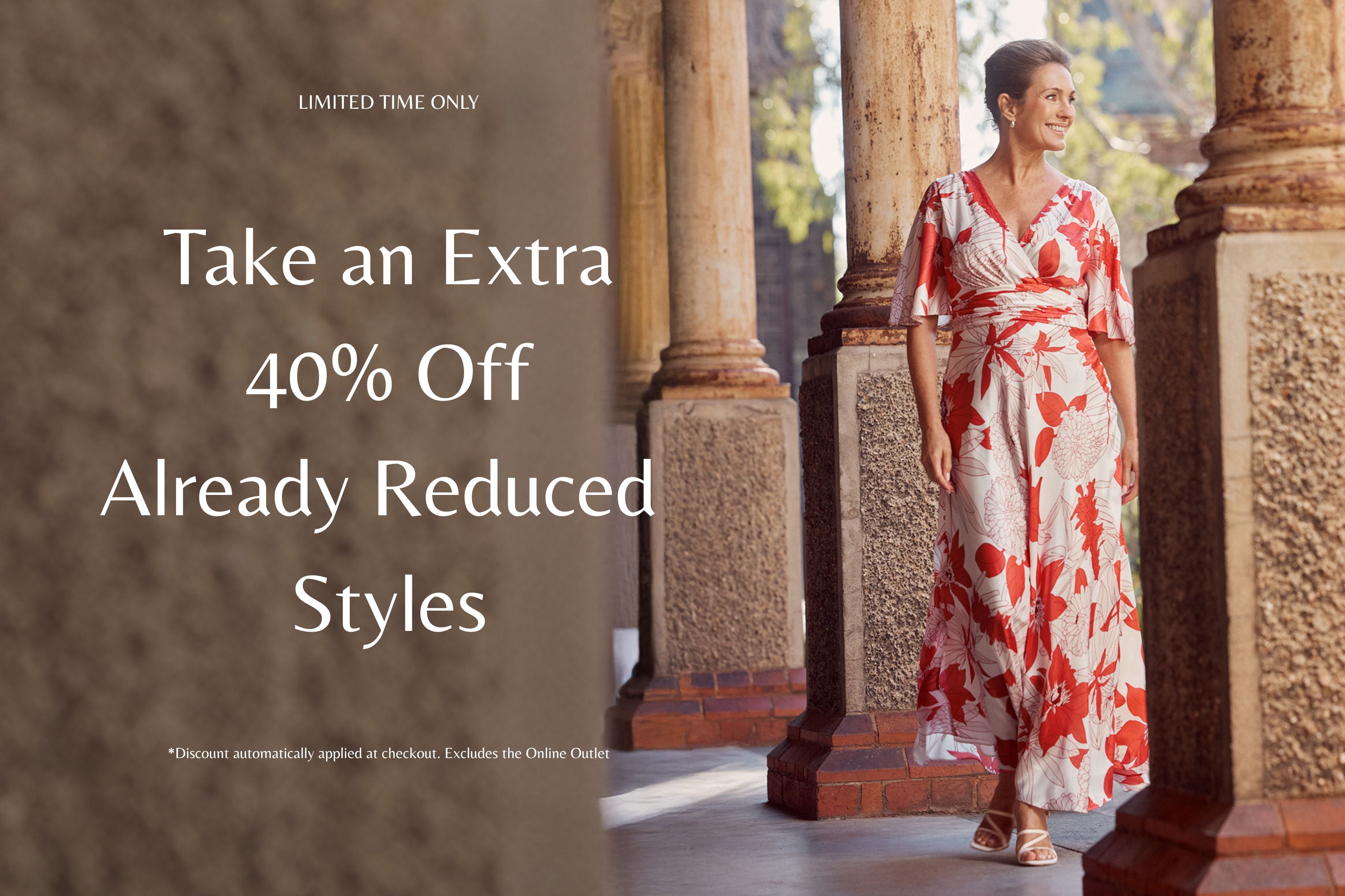 Woman in a floral dress standing in an outdoor setting with promotional text overlay. Take an Extra 40% Off Already Reduced Styles- Elena Vermilion Floral Gown.